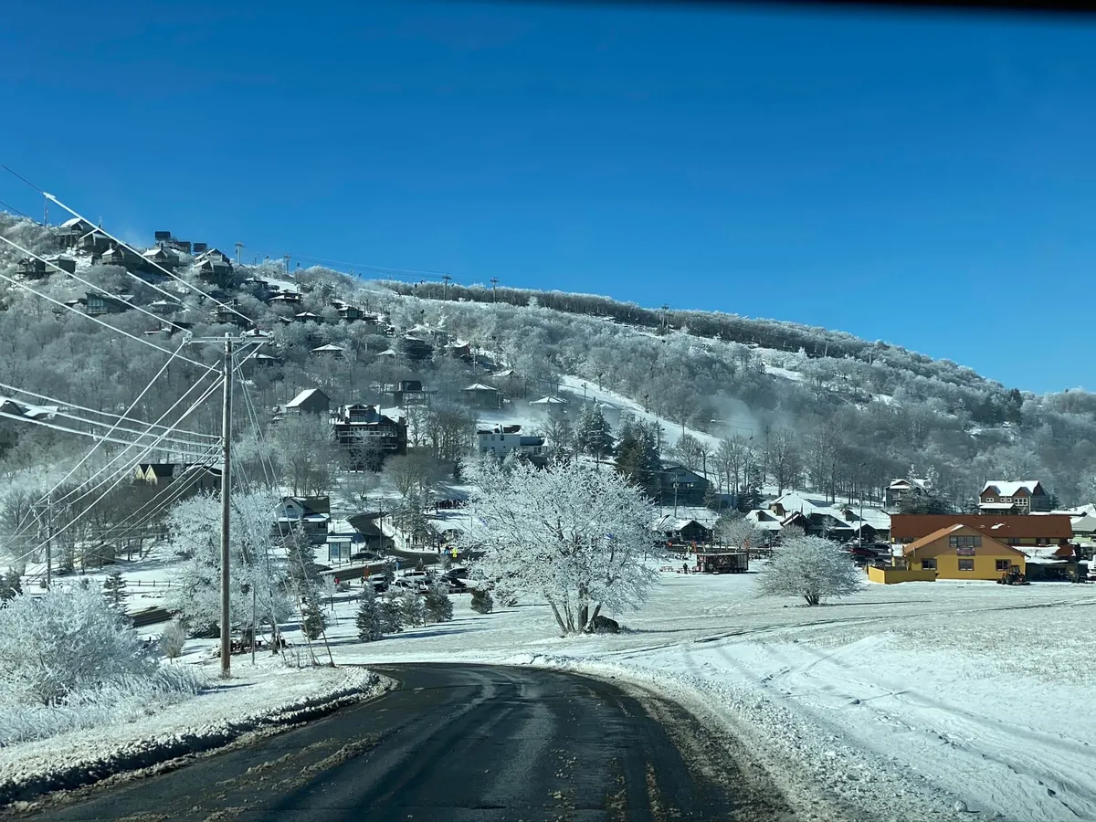 A serene panorama of snow-covered hills dotted with colorful houses, including a winding road and a tree draped in snow. The landscape invites exploration, offering a tranquil counterpoint to the activity in the previous image. The scene suggests opportunities for nature walks, scenic drives, and relaxation after a day of recreation.
